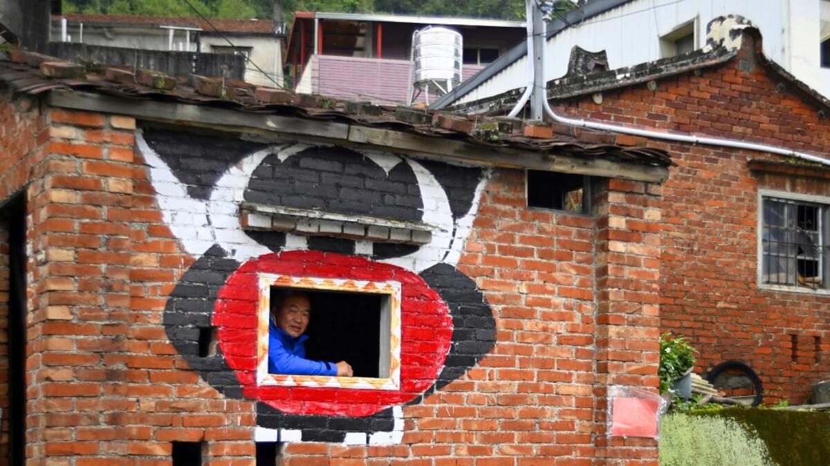 This picture taken on March 30, 2019 shows Hakka graffiti painter Wu Tsun-hsien posing for a photo in a empty old house near his home in the Taiwanese village of Ruan Chiao. Nestled in the mist-covered foothills of Taiwan's central mountain range, Ruan Chiao village is virtually devoid of young people, but artist Wu Tsun-hsien is coaxing the Instagram generation back by transforming local homes into a canvas of colour. Sam YEH / AFP