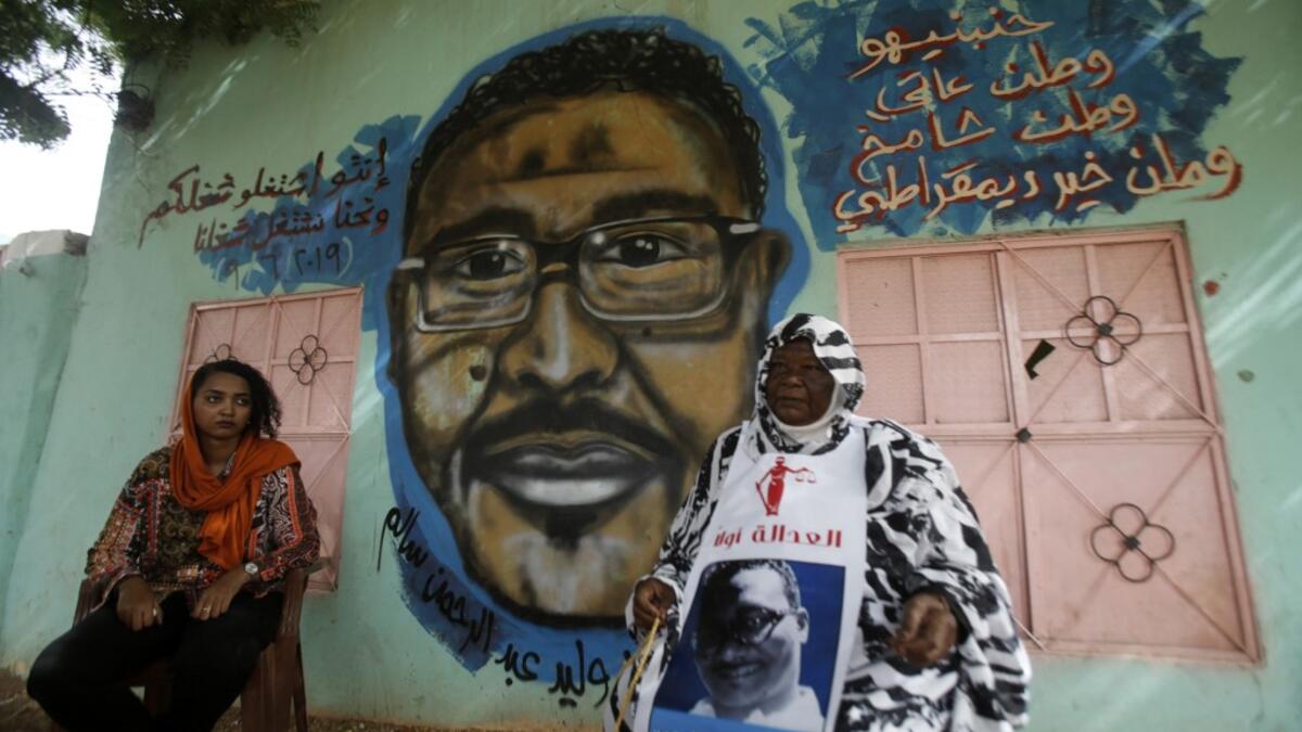 Maiyssa Omar (R), the mother of Walid Abdelrahim and Sudanese artist Assil Diab, sit in front of the mural painting of Abdelrahim ornating the family home in the capital Khartoum on July 21, 2019.  ASHRAF SHAZLY / AFP
