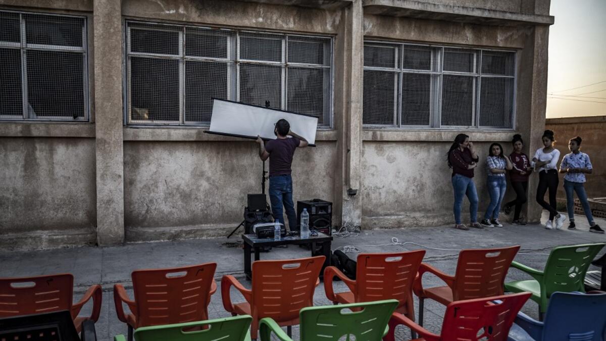 A member of Syrian-Kurdish filmmaker Shero Hinde's mobile cinema "Komina Film" initiative prepares a projector screen for a film screening for children at a school yard in the village of Shaghir Bazar, 55 kilometres southest of Qamishli in the Kurdish-populated areas of northeastern Syria's Hasakeh province, on July 28, 2019.  DELIL SOULEIMAN / AFP