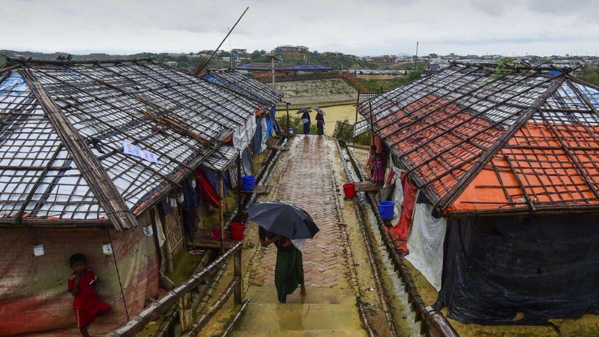 A Rohingya refugee girl shelters from the rain under an umbrella as she makes her way back home after collecting relief aid at the Kutupalong Rohingya refugee camp in Bangladesh's Ukhia district on August 24, 2019.  MUNIR UZ ZAMAN / AFP