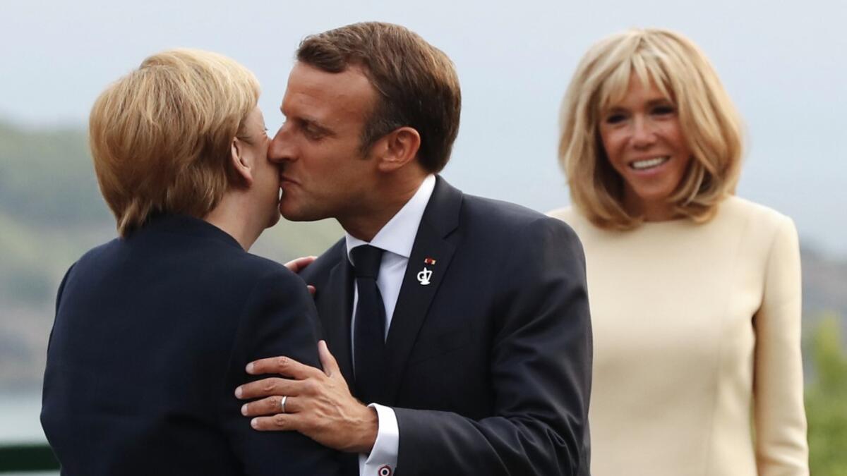 French President Emmanuel Macron (C) welcomes German Chancellor Angela Merkel with a kiss past his wife Brigitte Macron at the Biarritz lighthouse, southwestern France, ahead of a working dinner on August 24, 2019. Francois Mori / POOL / AFP