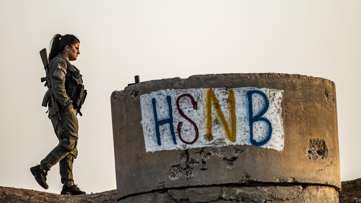 A member of the Bethnahrin Women Protection Forces (HSNB), an all-female Syriac-Assyrian paramilitary group under the umbrella of the Syrian Democratic Forces (SDF), walks past graffiti reading out the group's initials in Latin characters during a commemoration of the fourth anniversary of their creation, in the countryside of the town of Tall Tamr in the northwestern Syrian province of Hasakah, on August 30, 2019.  Delil SOULEIMAN / AFP