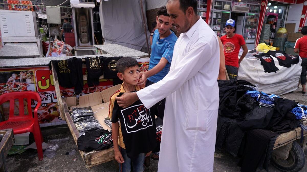 A man tries on a black t-shirt on the chest of a child, emblazoned with the Shiite Muslim slogan "O Abbas", as a sign of mourning referring to the Muslim Imam Abbas ibn Ali, grandson of the prophet Mohamed, amidst preparations ahead of the Shiite Muslim religious mourning period of Ashura, in the central Iraqi holy shrine city of Najaf on August 31, 2019.  Haidar HAMDANI / AFP
