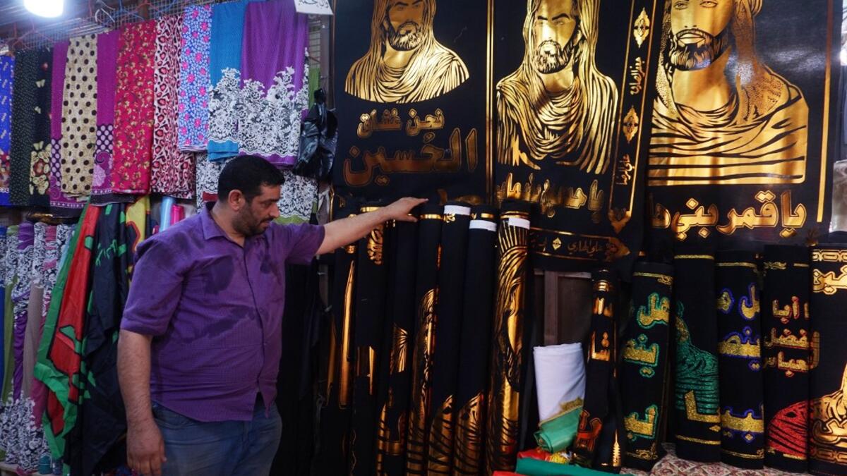 A man stands next to cloth banners depicting Shiite Muslim Imams Hussein ibn Ali (L and C) and his brother Abbas ibn Ali (R), grandsons of the prophet Mohammed, to be sold amidst preparations ahead of the Shiite Muslim religious mourning period of Ashura, in the central Iraqi holy shrine city of Najaf on August 31, 2019.  Haidar HAMDANI / AFP