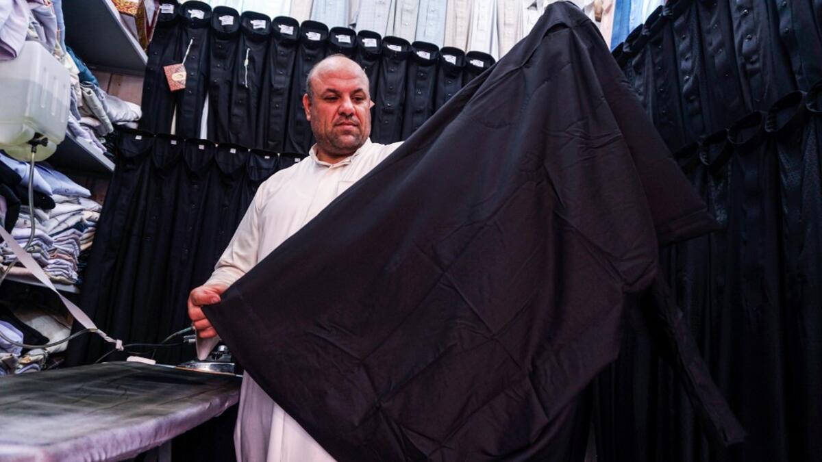 A man showcases a black garb in a shop lined-up with black and other coloured shirts, to be sold to Shiite Muslim pilgrims amidst preparations ahead of the Shiite religious mourning period of Ashura in the central Iraqi holy shrine city of Najaf on August 31, 2019.  Haidar HAMDANI / AFP