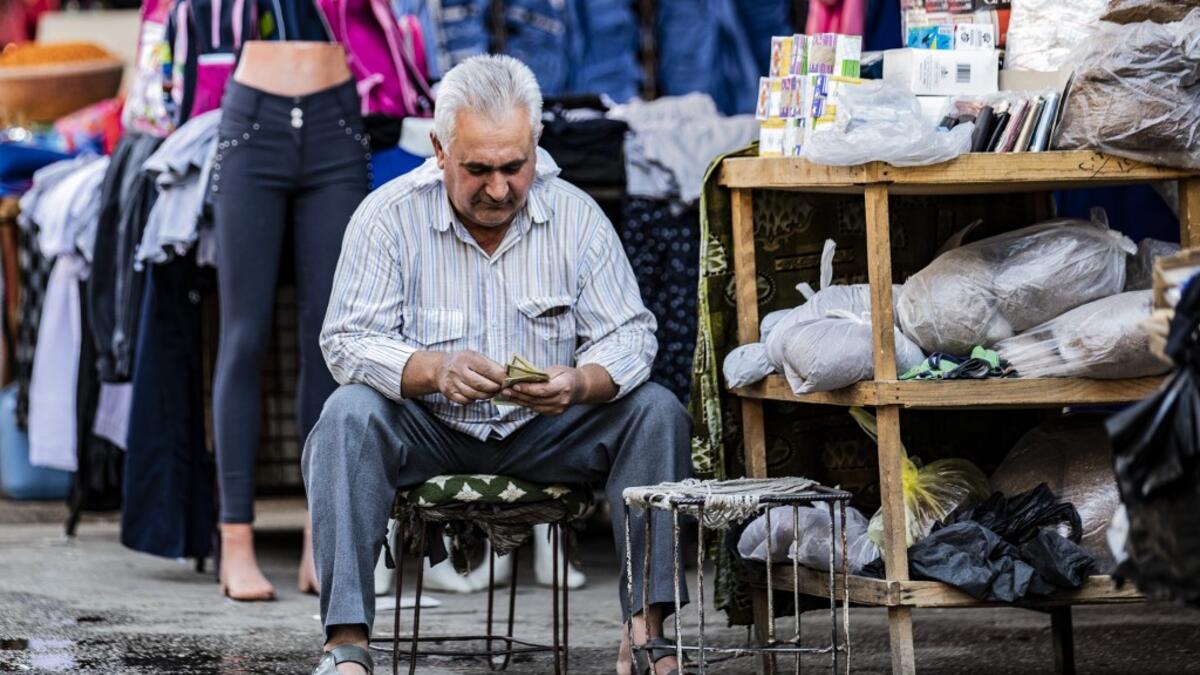 A merchant counts money in front of his shop at a market in the Kurdish-majority city of Qamishli in northeast Syria on  Delil SOULEIMAN / AFP