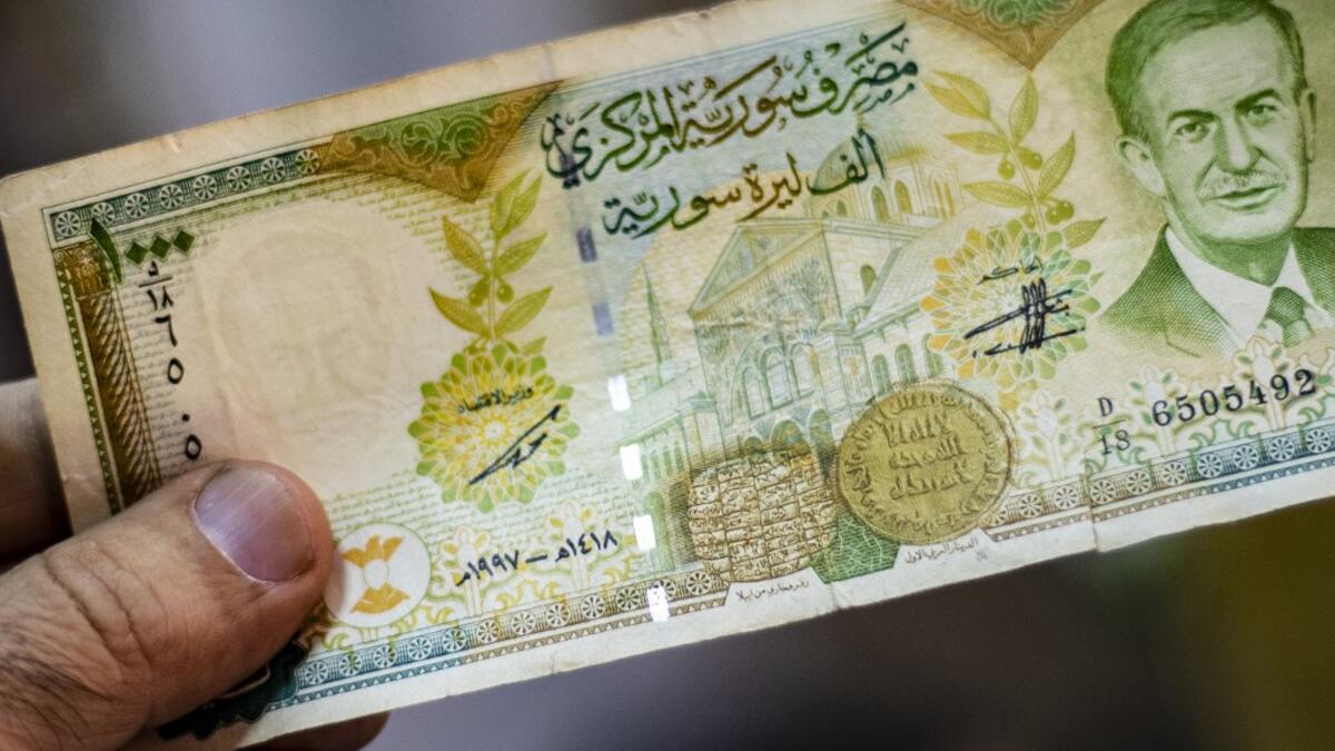 A merchant holds a Syrian pound note, bearing a portrait of late Syrian President Hafez al-Assad, at a market in the Kurdish-majority city of Qamishli in northeast Syria.  Delil SOULEIMAN / AFP