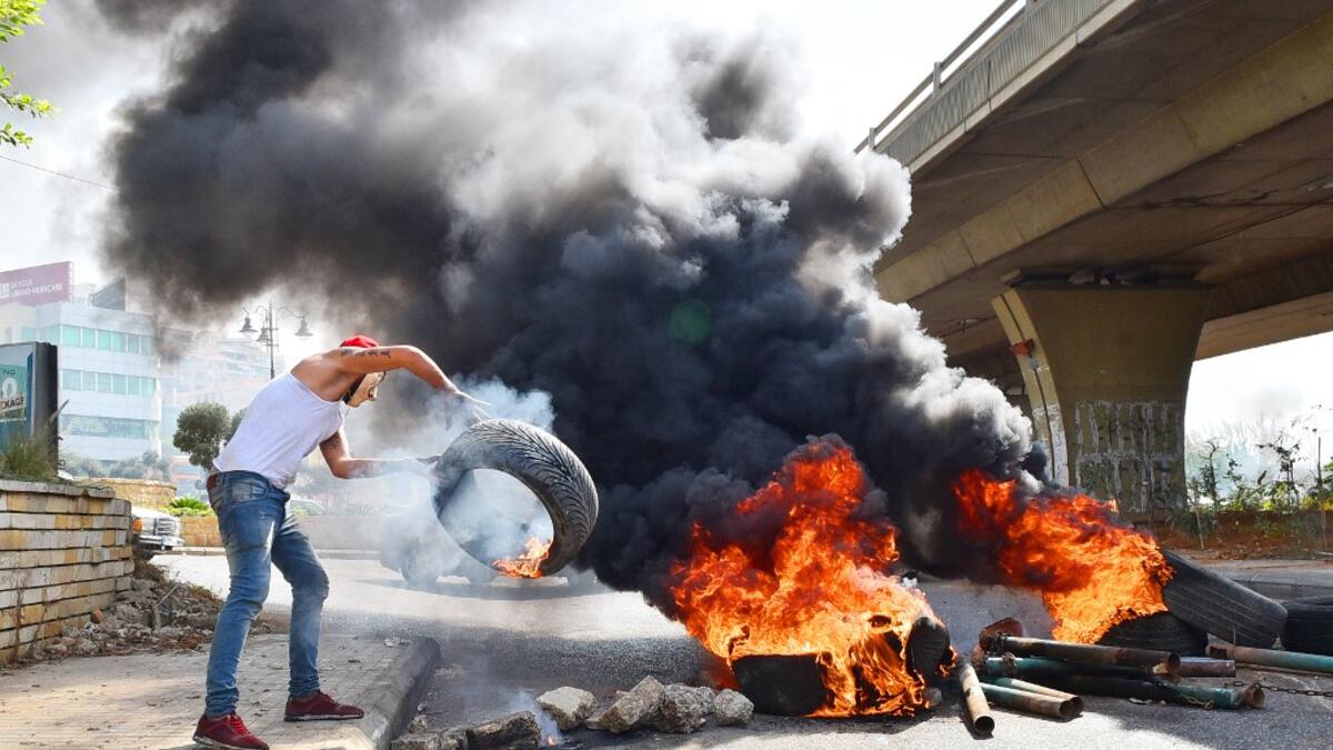 A Lebanese protester throws a tire into a fire blocking a road near Beirut-Rafic Hariri International Airport, amidst ongoing protests against dire economic conditions, on October 18, 2019. Public anger has simmered since parliament passed an austerity budget in July to help trim a ballooning deficit and flared on October 17 over new plans to tax calls on messaging applications such as WhatsApp, forcing the government to axe the unpopular proposal. AFP