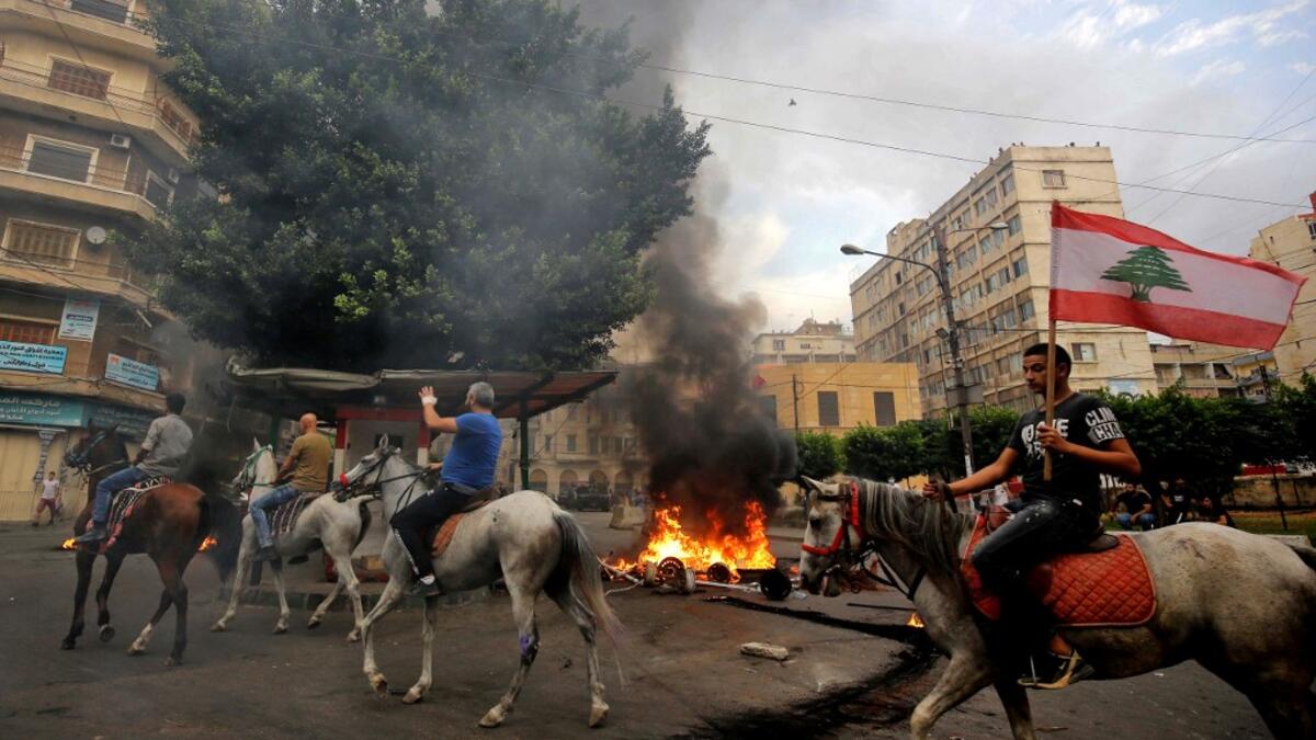 Lebanese protesters ride horses past burning tires in front of the house of former sports minister Faisal Karami, during a protest against dire economic conditions in the coastal city of Tripoli to the north of Beirut, Lebanon on October 18, 2019 Ibrahim CHALHOUB / AFP