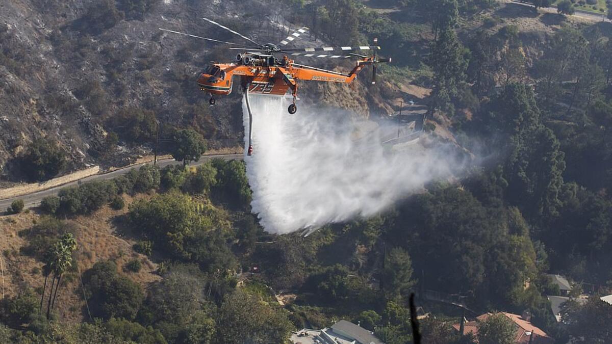 A helicopter drops water on houses on fire in Brentwood on Monday as fires continue to ravage California. (AFP)