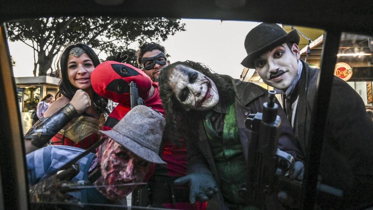 Venezuelan migrant Johnny Tales (2-R), who makes a living imitating the comicbook and film character "The Joker", performs at a street with fellow compatriots also fancy dressed as comic and film industry characters in Medellin, on October 29, 2019. JOAQUIN SARMIENTO / AFP