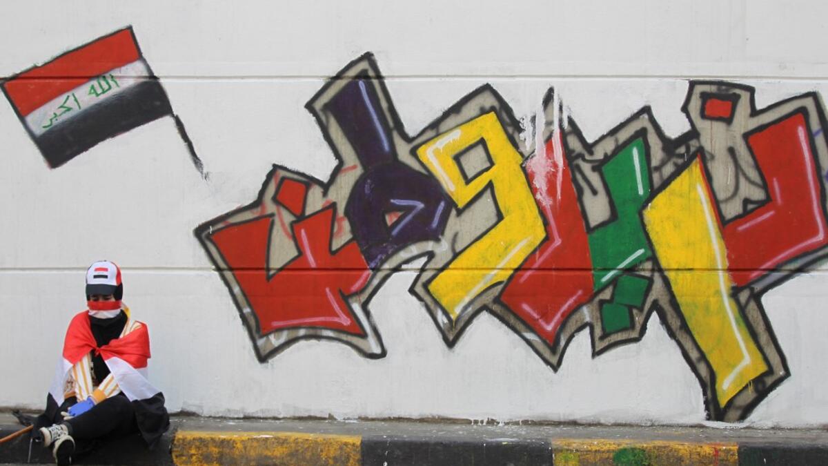 An Iraqi demonstrator clad with the national flag rests in front of a mural which reads "we want a homeland", amid ongoing anti-government protests in the capital Baghdad on November 3, 2019. Protesters in Iraq's capital and the country's south shut down streets and government offices in a new wave of civil disobedience, escalating their month-long movement demanding wholesale change of the political system. AHMAD AL-RUBAYE / AFP