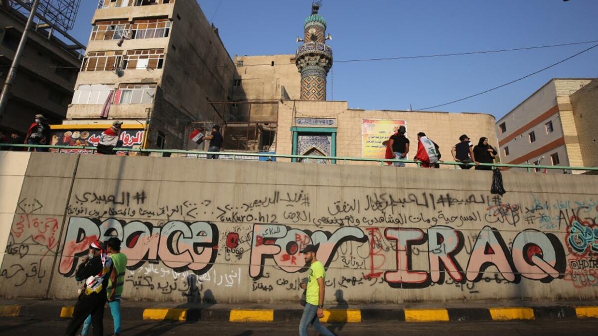 Iraqi demonstrators walk by a graffiti-filled wall in Tahrir square in the capital Baghdad on November 3, 2019, amid ongoing anti-government protests. Protesters in Iraq's capital and the country's south shut down streets and government offices in a new wave of civil disobedience, escalating their month-long movement demanding wholesale change of the political system. AHMAD AL-RUBAYE / AFP