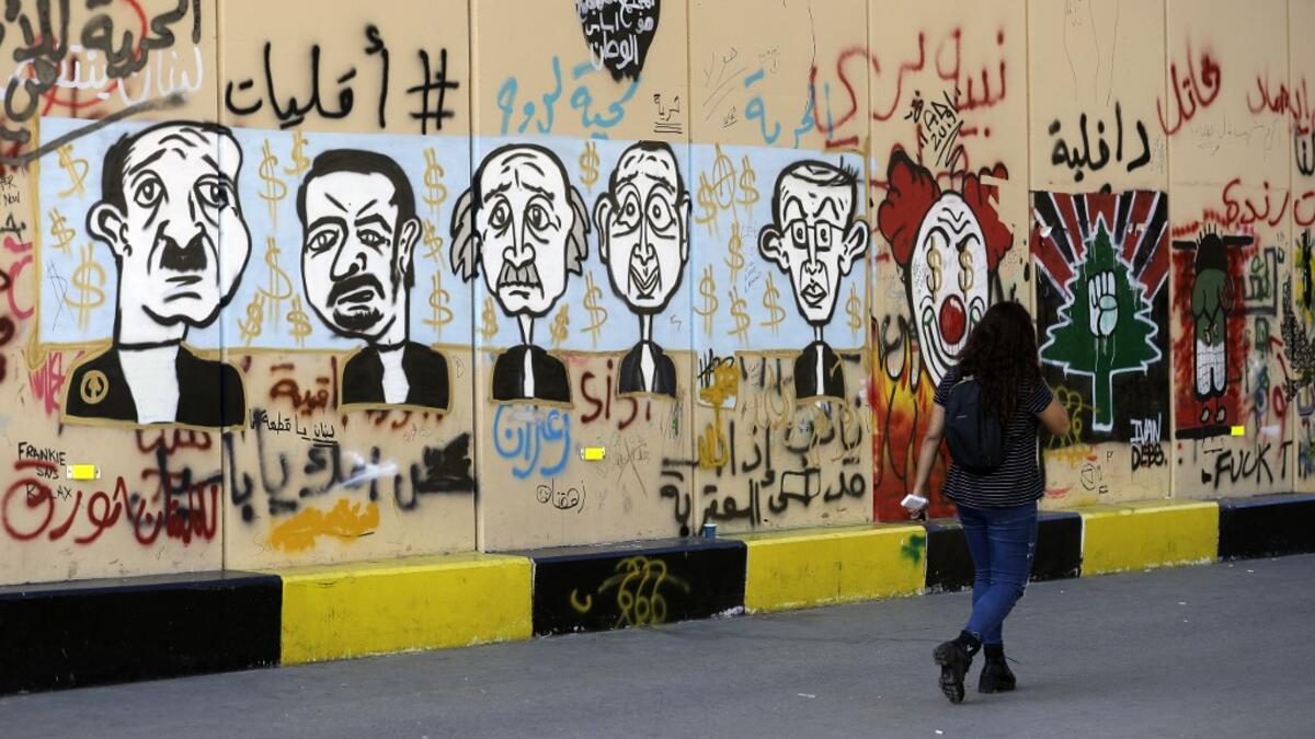 A woman walks past graffitis sprayed on a wall in Lebanon's capital Beirut on November 6, 2019. Since October 17, the chanting of tens of thousands of Lebanese denouncing the political elite have shaken the normally staid district around two Beirut squares, Martyrs' and Riad Al Solh. JOSEPH EID / AFP
