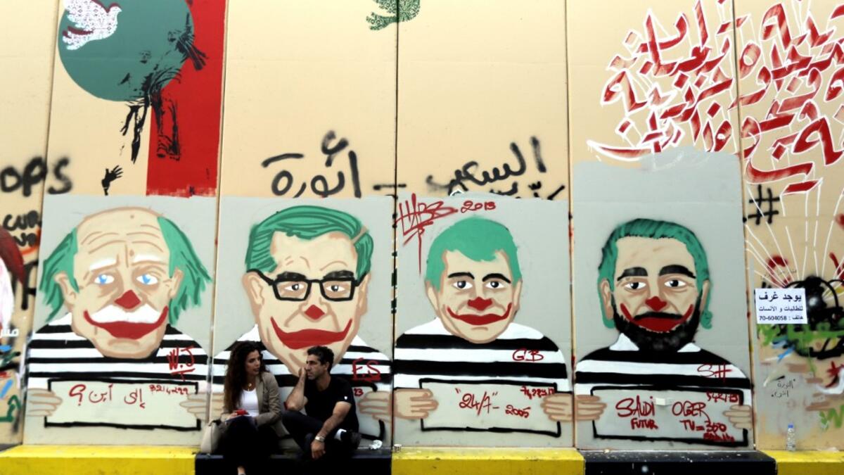 Anti-government protesters sit under graffiti depicting Lebanese politicians with joker faces sprayed on a wall in downtown Beirut on November 12, 2019. Banks and schools in Lebanon were closed today as protesters tried to prevent employees from clocking in at state institutions nearly one month into an anti-graft street movement. Unprecedented protests erupted across Lebanon on October 17, demanding the ouster of a generation of politicians seen by demonstrators as inefficient and corrupt.  JOSEPH EID / AF