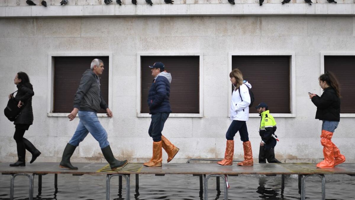 People walk on a footbridge across a flooded street after an exceptional overnight "Alta Acqua" high tide water level, on November 13, 2019 in Venice. Venice was hit by the highest tide in more than 50 years late November 12, with tourists wading through flooded streets to seek shelter as a fierce wind whipped up waves in St. Mark's Square. Marco Bertorello / AFP