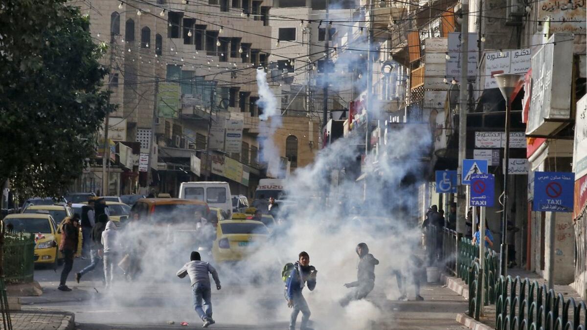 Palestinian youths run from tear gas smoke fired by Israeli security forces on November 26, 2019 during clashes in the West Bank city of Hebron during a Palestinian "day of rage" against a recent US decision to no longer consider settlements in the West Bank illegal. A Palestinian convicted over the killing of three Israelis died of cancer in custody today, officials said. The death, which sparked Palestinian accusations of neglect, comes amid heightened tension with protests already scheduled in multiple p