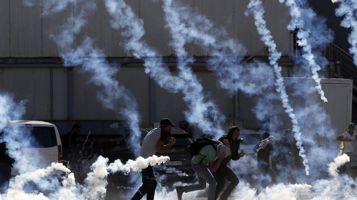 Palestinian youths run from tear gas smoke fired by Israeli security forces on November 26, 2019 during clashes in the West Bank city of Ramallah as Palestinians stage a "day of rage" against a recent US decision to no longer consider settlements in the West Bank illegal. A Palestinian convicted over the killing of three Israelis died of cancer in custody today, officials said. The death, which sparked Palestinian accusations of neglect, comes amid heightened tension with protests already scheduled in multi