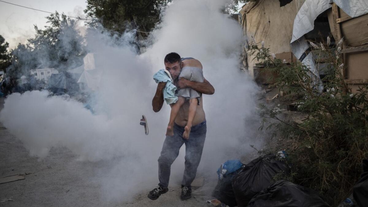A man holds a boy during clashes with police outside the refugee camp of Moria on the Greek island of Lesbos, on September 29, 2019. At least one migrant died on September 29, 2019, after a fire broke out in Moria, the over-crowded refugee camp on the Greek island of Lesbos, Greece's Health Ministry said. Police were firing tear gas to control crowds who started rioting after the fire ignited inside the camp, according to an AFP correspondent. ANGELOS TZORTZINIS / AFP