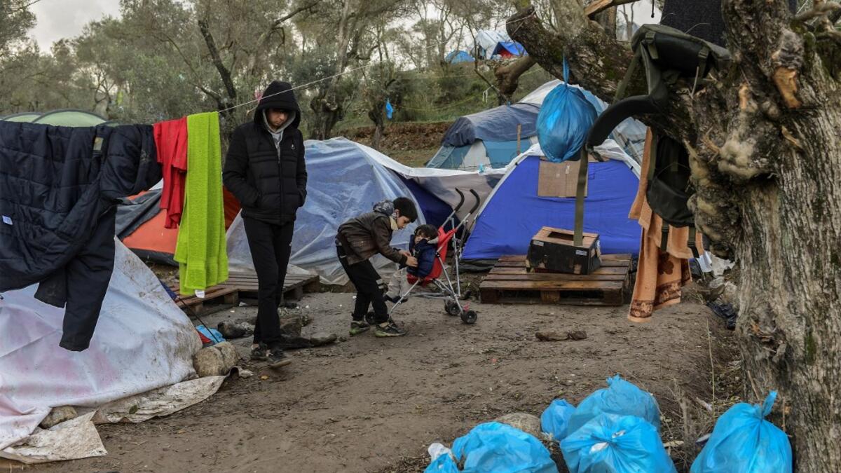 A young boy puts a jacket on his brother at the makeshift camp next to the refugee camp of Moria near the capital Mytilene in the island of Lesbos on November 29, 2019. ARIS MESSINIS / AFP