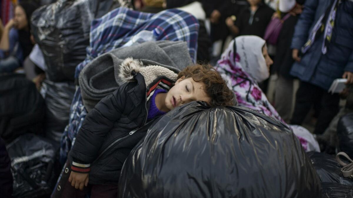 A child rests on bags as migrants and refugees wait to depart from the Greek island camp of Moria on Lesbos to Athens on November 29, 2019.ARIS MESSINIS / AFP