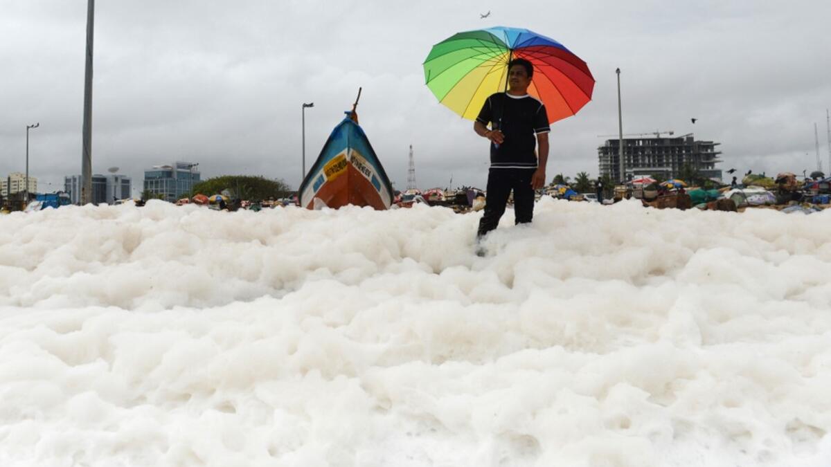 A man holds an umbrella over foamy discharge, caused by pollutants, as it mixes with the surf at Marina beach in Chennai on December 1, 2019. Arun SANKAR / AFP
