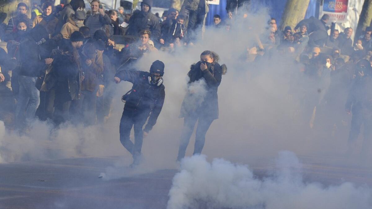 A man throws a tear canister back as people stand amid tear gas smoke during a demonstration against the pension overhauls, in Bordeaux, on December 5, 2019, as part of a national general strike. NICOLAS TUCAT / AFP