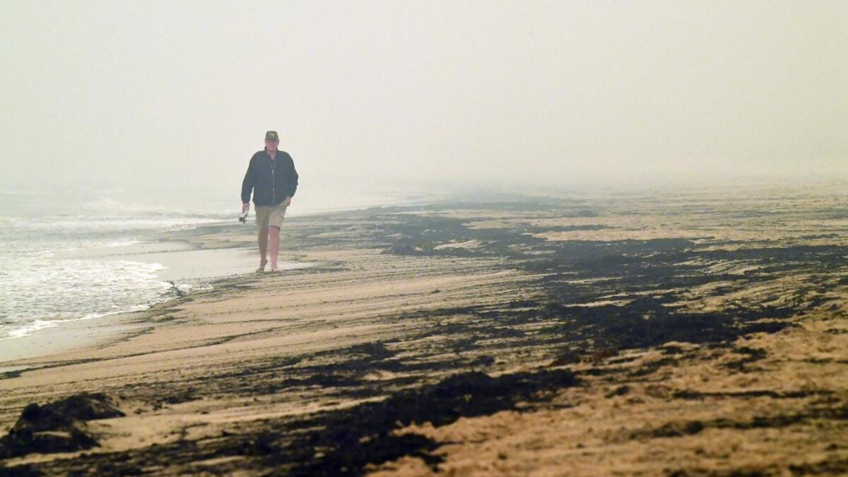 Local resident Dave Iredale walks past ash from bushfires washed up on a beach in Merimbula, in Australia's New South Wales state on January 5, 2020. Australians on January 5 counted the cost from a day of catastrophic bushfires that caused "extensive damage" across swathes of the country and took the death toll from the long-running crisis to 24. SAEED KHAN / AFP