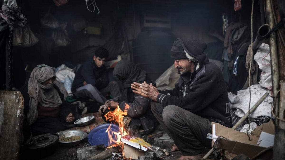 Members of a Palestinian family warm themselves by a fire during a cold weather spell in an empoverished neighbourhood on the outskirts in Gaza City on January 9, 2020. MAHMUD HAMS / AFP