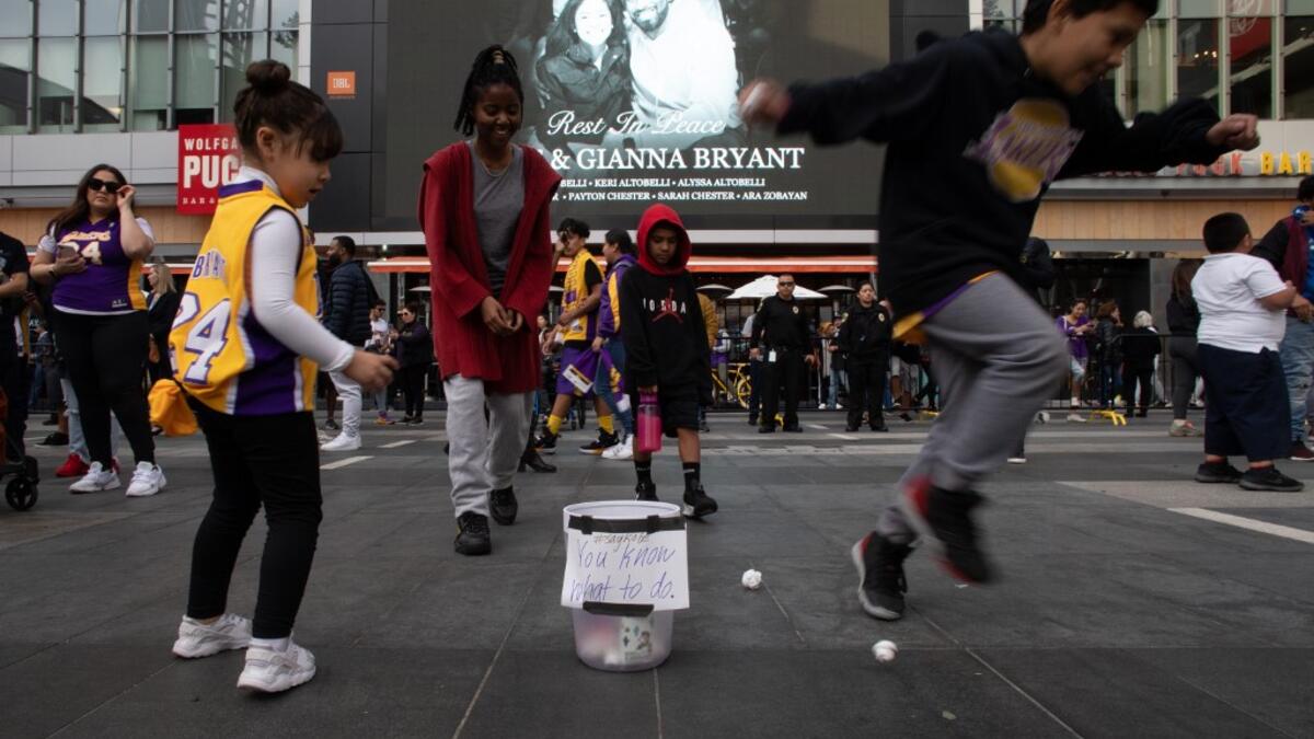 Children plays basket with paper balls in a trash can in front of a makeshift memorial for former NBA and Los Angeles Lakers player Kobe Bryant and his daughter Gianna Bryant, who were killed with seven others in a helicopter crash on January 26, at LA Live plaza in front of Staples Center in Los Angeles on January 27, 2020. Federal investigators sifted through the wreckage of the helicopter crash that killed basketball legend Kobe Bryant and eight other people, hoping to find clues to what caused the accid