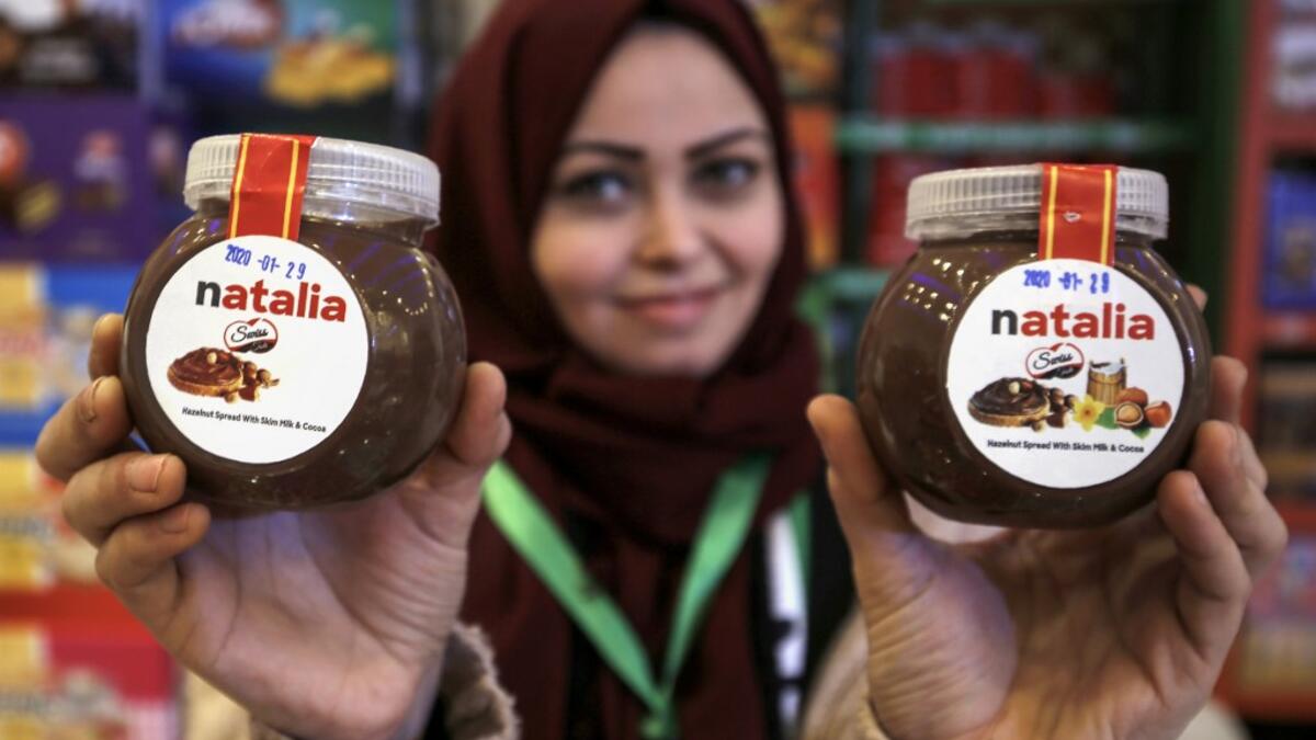 A shop employee holds up jars of a Gazan version of a world famous spread, dubbed 'Natalia', in Gaza city on February 12, 2020. Al-Arees's products are Gazan but their components are not, as few of the basic raw ingredients are produced in the impoverished Mediterranean coastal strip. MOHAMMED ABED / AFP