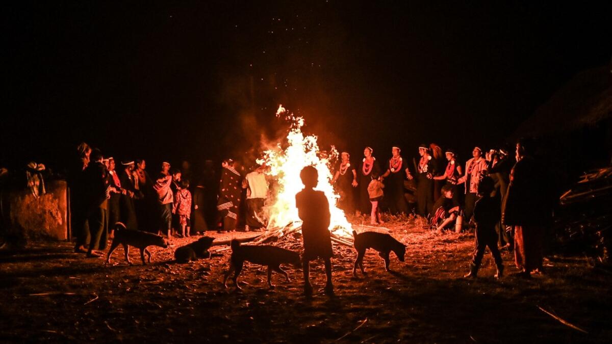 This photo taken on February 6, 2020 shows a child standing with dogs by a fire as Naga tribeswomen take part in an overnight ceremony to bless the harvest in Satpalaw Shaung village, Lahe township in Myanmar's Sagaing region. A haunting refrain pierces the night as the tribeswomen of the Gongwang Bonyo, among the most isolated people in Myanmar, dance around a campfire to bless the harvest ahead. YE AUNG THU / AFP