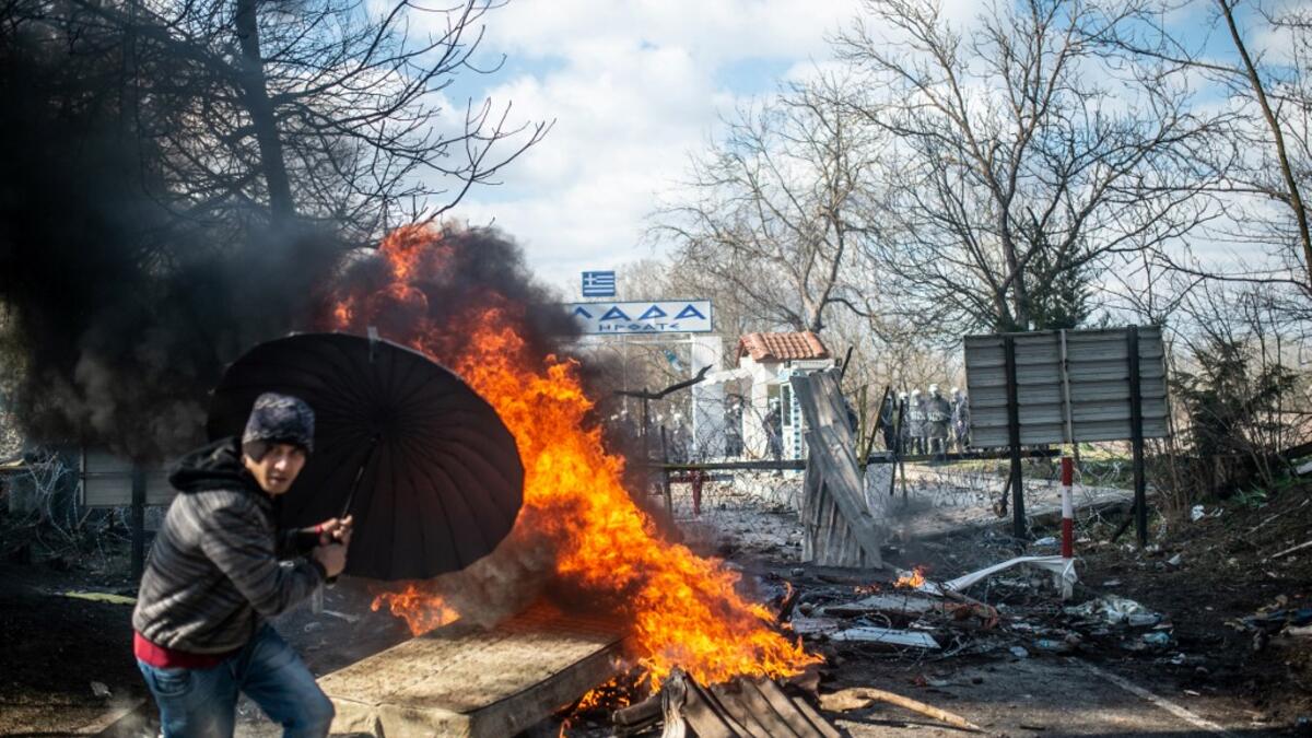 A man takes coover behind an umbrella as he throws a mattress in a fire during clashes with Greek police in the buffer zone at Turkey-Greece border, at Pazarkule, in Edirne district, on February 29, 2020. BULENT KILIC / AFP