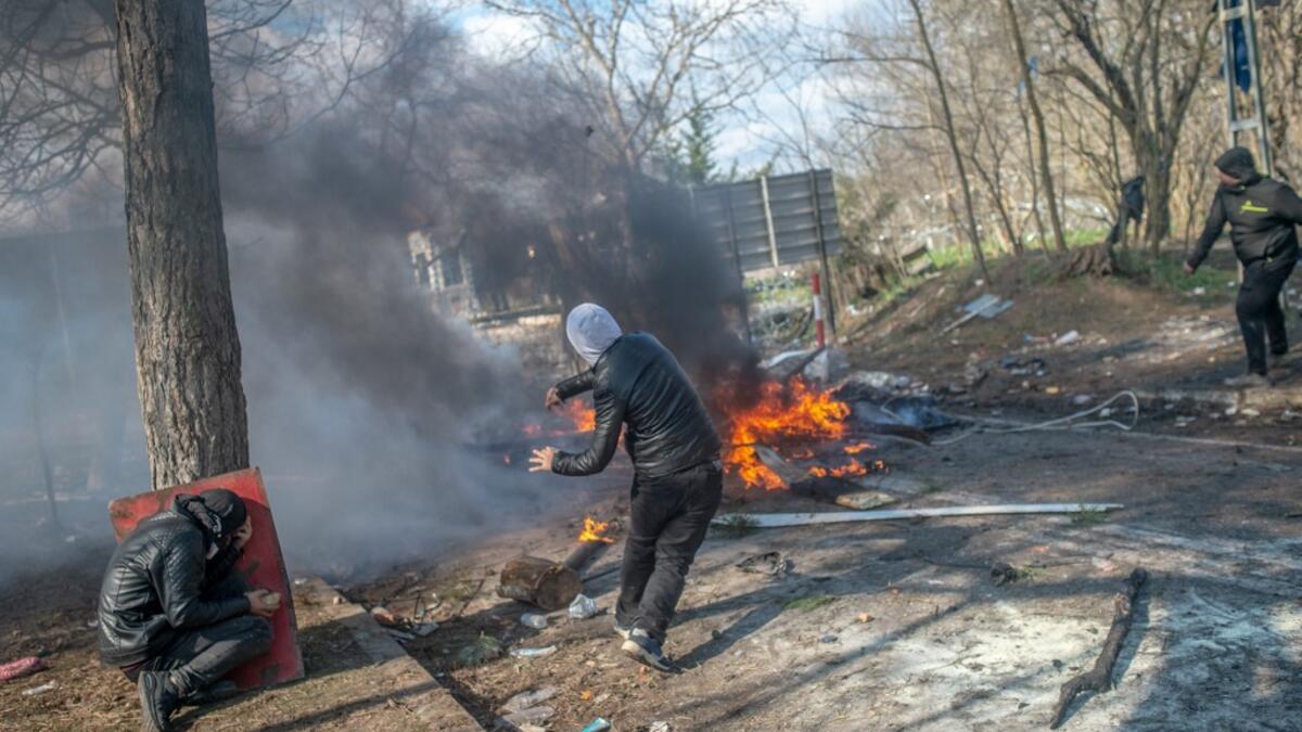 A man throws a stone to Greek police as another takes cover behind a tree during clashes in the buffer zone at Turkey-Greece border, at Pazarkule, in Edirne district, on February 29, 2020. Thousands of migrants stuck on the Turkey-Greece border clashed with Greek police on February 29, 2020, according to an AFP photographer at the scene. BULENT KILIC / AFP
