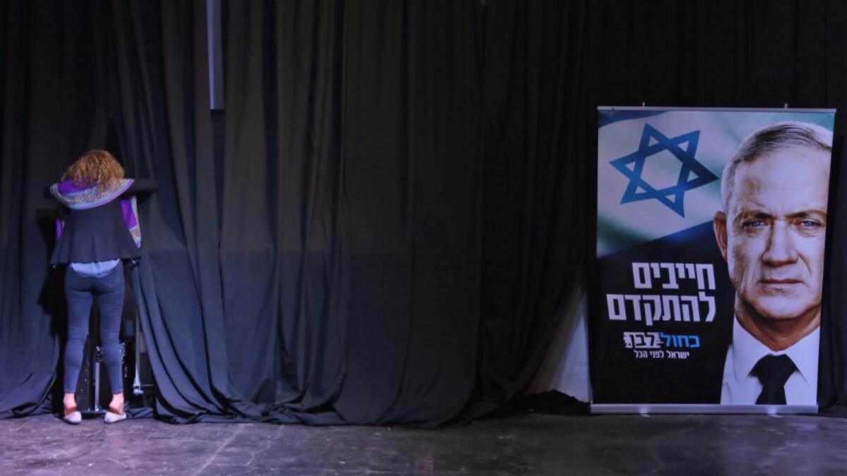 A woman stands in front of curtains at a stage near a sign showing the face of the Blue and White (Kahol Lavan) alliance's leader Benny Gantz, with text in Hebrew reading "we must move forward", at the alliance's electoral headquarters in the coastal city of Tel Aviv early on March 3, 2020. GALI TIBBON / AFP