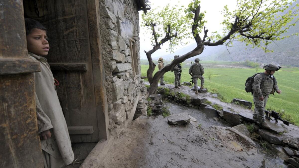 In this file photo taken on April 8, 2009, an Afghan boy watches US soldiers from 1st Infantry Division patrolling in a village during a mission of searching weapon cache in Nishagam, in Afghanistan's eastern Kunar province. American forces have started pulling out of two bases in Afghanistan, a US official said on March 10, 2020 the day peace talks between Kabul and the Taliban were due to start despite widespread violence and a political crisis. The United States is keen to end its longest-ever conflict,
