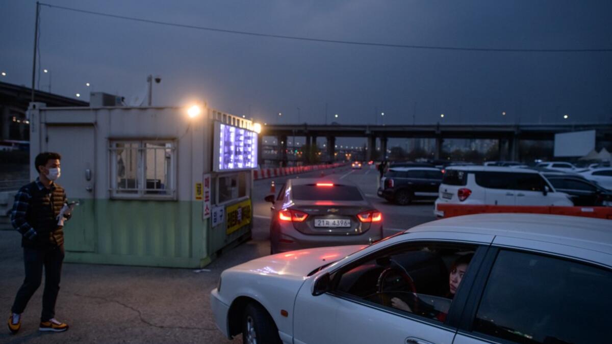 In a photo taken on March 21, 2020 customers queue in their cars to buy tickets at a drive-through cinema in Seoul. Box office numbers in South Korea -- which has 8,897 confirmed virus cases -- have plummeted in recent weeks due to the epidemic, with authorities urging the public to avoid large crowds. But at drive-in cinemas, moviegoers can enjoy a movie from the comfort of their cars, parked in front of a large outdoor screen.  Ed JONES / AFP