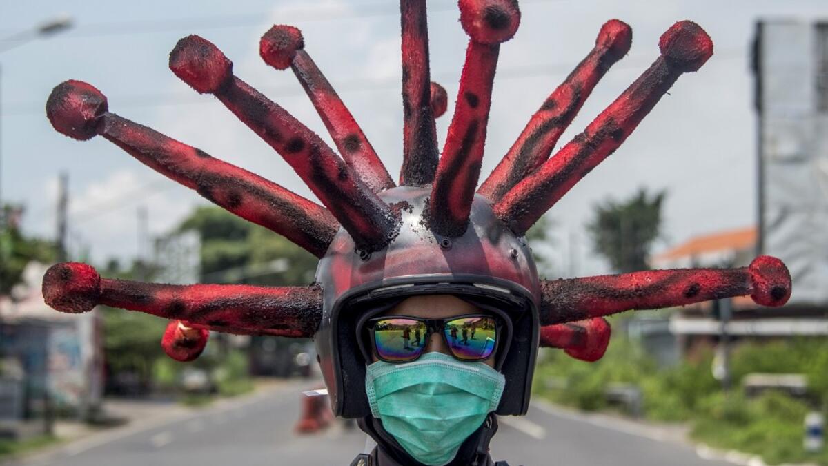 An Indonesian police officer wearing a Covid-19 coronavirus themed helmet conducts a campaign and disinfects motorists' vehicles in Mojokerto, East Java on April 3, 2020. Juni Kriswanto / AFP