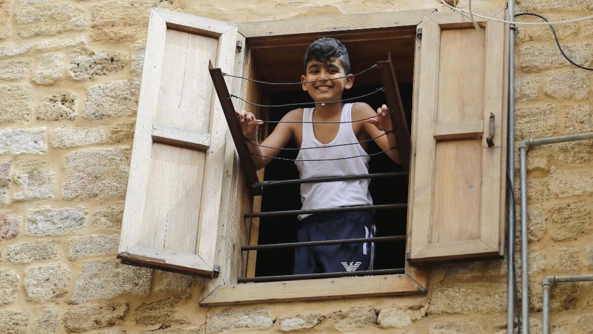 A Lebanese boy smiles as he looks out of a window during confinement at home due to the COVID-19 pandemic, in the historic part of the southern coastal city of Sidon (Saida), on April 6, 2020. Lebanon's President called on international donors to provide financial assistance to the crisis-hit country as it grapples with a severe economic downturn compounded by the novel coronavirus pandemic. JOSEPH EID / AFP