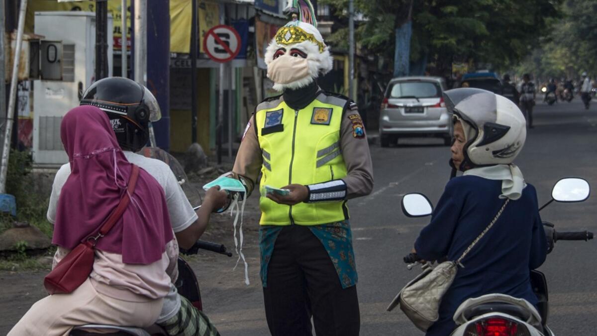 A police officer wearing a Indonesian a superhero costume on the street gives face masks to motorists in Pasuruan, East Java on April 9, 2020, amid concert to the COVID-19 coronavirus. JUNI KRISWANTO / AFP