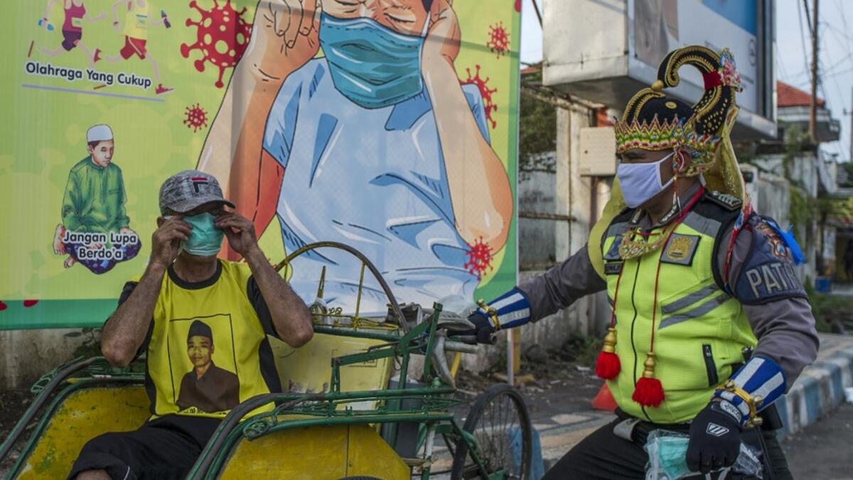 An Indonesian police officer wearing an Indonesian superhero costume on the street gives a face mask to a man in Pasuruan, East Java on April 9, 2020, amid concert to the COVID-19 coronavirus. JUNI KRISWANTO / AFP
