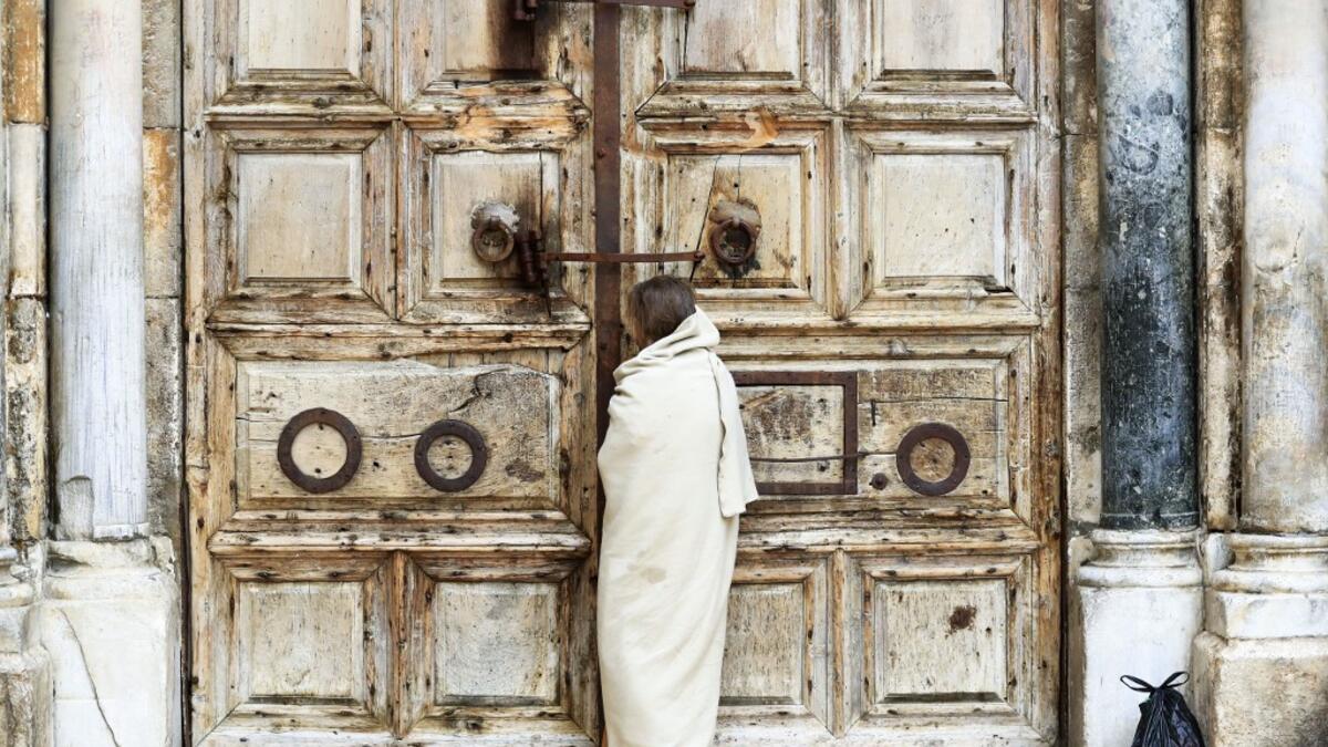 A Christian pilgrim dressed as Jesus Christ stands in front of the closed door of the Holy Sepulchre Church in Jerusalem's Old City on April 10, 2020, marking Good Friday, amid the COVID-19 pandemic crisis. All cultural sites in the Holy Land are shuttered, regardless of their religious affiliation, as authorities seek to forestall the spread of the deadly respiratory disease, which will prevent Christians from congregating for the Easter service, this coming Sunday for Catholic worshippers, then a week lat
