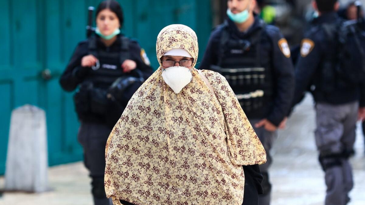 A woman wearing a protective mask amid the COVID-19 outbreak, makes her way along the Via Dolorosa while Israeli policemen patrol the mostly empty route, during Good Friday in Jerusalem, on April 10, 2020. All cultural sites in the Holy Land are shuttered, regardless of their religious affiliation, as authorities seek to forestall the spread of the deadly respiratory disease, which will prevent Christians from congregating for the Easter service, this coming Sunday for Catholic worshippers, then a week late