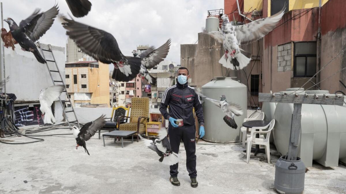 A pigeon owner, wearing personal protective equipment, watches his pigeons fly on the rooftop of his building in the southern suburb of Beirut on April 11, 2020. ANWAR AMRO / AFP