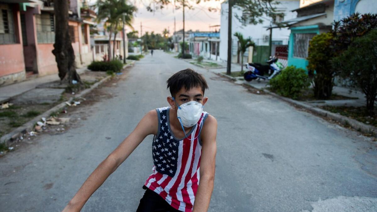 A youngster wearing a shirt with the US flag and a face mask, rides a bicycle in Havana, on April 13, 2020. While Cuba tries to stop the spread of the coronavirus on the island, with 726 cases, voices can be heard to demand the lifting of the US embargo to facilitate the arrival of medical products. YAMIL LAGE / AFP