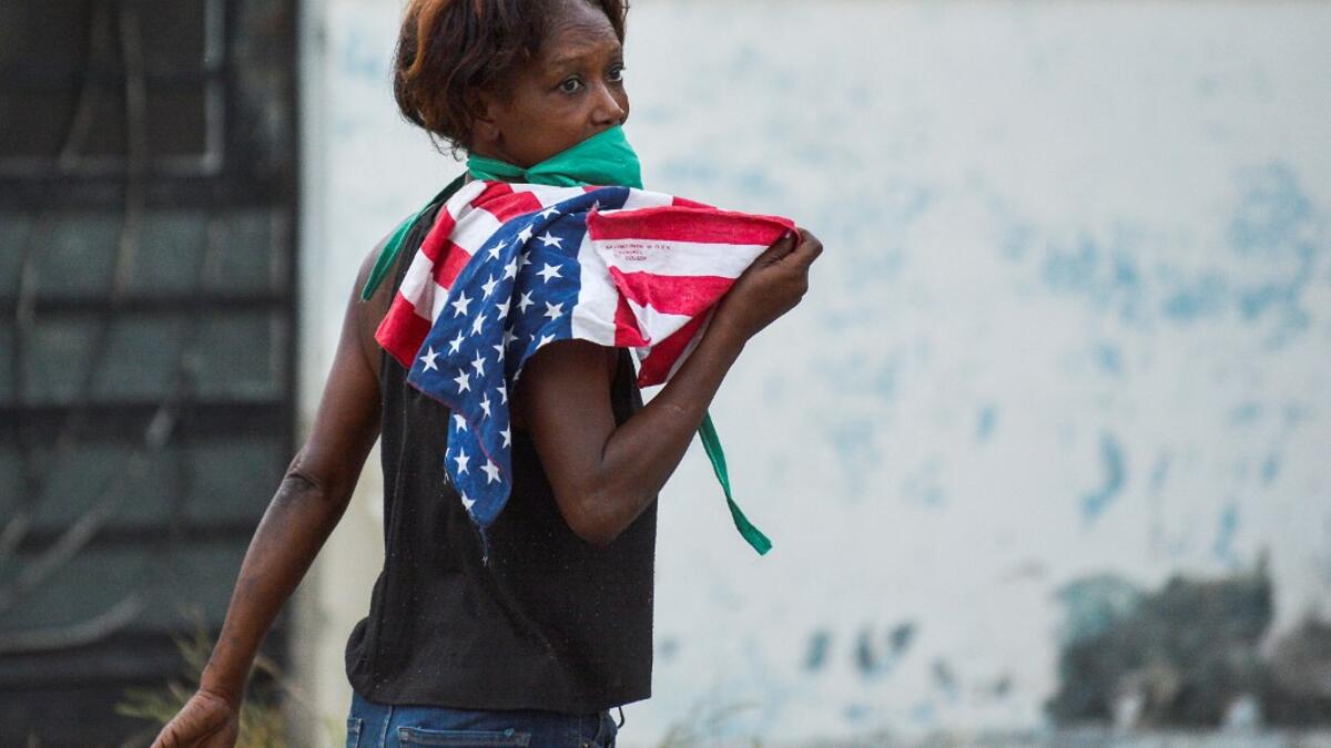 A woman wearing a face mask holds a US flag as she walks along a street in Havana, on April 13, 2020. While Cuba tries to stop the spread of the coronavirus on the island, with 726 cases, voices can be heard to demand the lifting of the US embargo to facilitate the arrival of medical products. YAMIL LAGE / AFP
