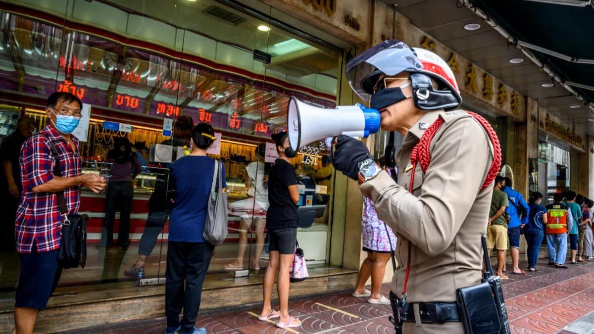 A police officer enforces social distancing as people wearing face masks amid fears of the spread of COVID-19 coronavirus line up to sell their jewelries in front of a gold shop in Bangkok's Chinatown on April 15, 2020. Hundreds of Bangkok residents rushed to goldsmith shops in order to sell their jewelries as gold prices reached its highest levels since 2012. Mladen ANTONOV / AFP