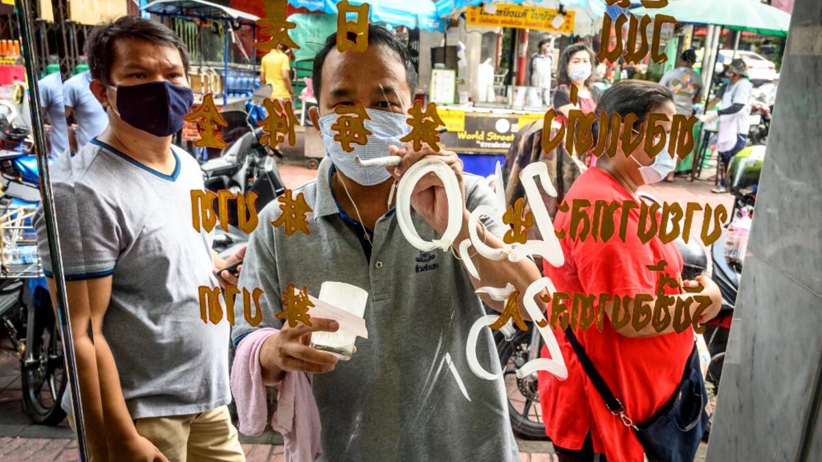 An employee wearing a face mask amid fears of the spread of COVID-19 coronavirus paints the new prices of gold on the shop window of a goldsmith in Bangkok's Chinatown on April 15, 2020. Hundreds of Bangkok residents rushed to goldsmith shops in order to sell their jewelries as gold prices reached its highest levels since 2012. Mladen ANTONOV / AFP