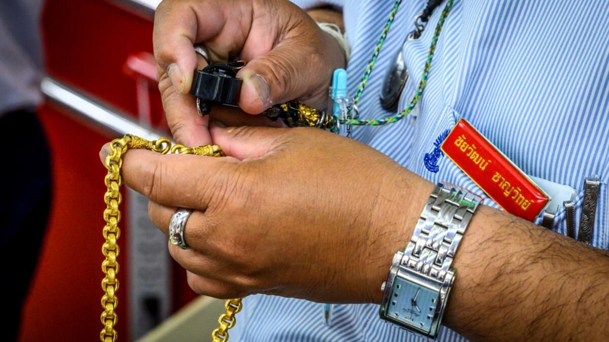 An employee checks a gold chain offered for sale in a gold shop in Bangkok's Chinatown on April 15, 2020. Hundreds of Bangkok residents rushed to goldsmith shops in order to sell their jewelries as gold prices reached its highest levels since 2012. Mladen ANTONOV / AFP