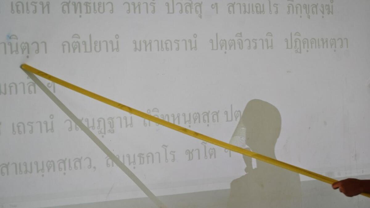A novice monks wearing a face shield as a preventive measure against the spread of the COVID-19 coronavirus reads religious text off a projection during religious studies at Wat Molilokkayaram Buddhist temple in Bangkok on April 20, 2020. Lillian SUWANRUMPHA / AFP